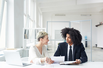 Contemporary economists discussing financial papers or contracts by workplace in office