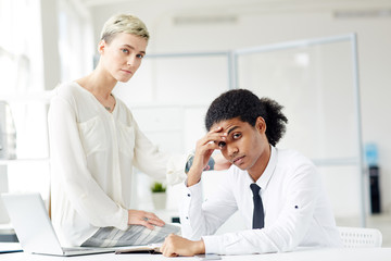 Upset intercultural colleagues looking at camera during work in office
