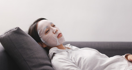Woman applying facial mask on sofa