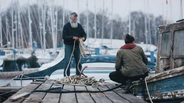  Father & son fishermen with battered old boat mooring it to jetty & chatting