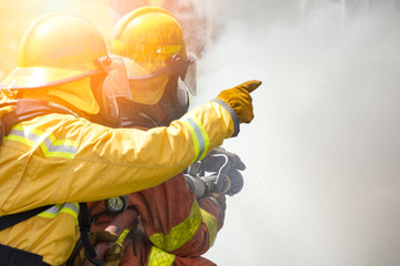 Fototapeta premium two firefighters water spray by high pressure nozzle to fire surround by smoke with flare and copy space