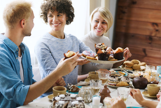 Helpful man giving plate with fresh pastry to his friends by festive table