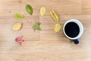 Autumn background with a cup of warming coffee, that stands on a wooden table and decorated with autumn leaves