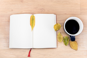 Autumn background with a cup of warming coffee, that stands on a wooden table and decorated with autumn leaves