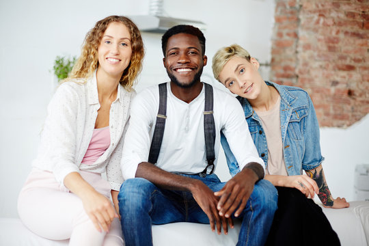 Happy young girls and African-american guy sitting on sofa