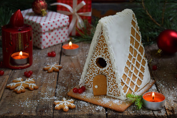 Homemade gingerbread house with pine branches, cones and biscuits on dark background. European Christmas traditions. Xmas holiday sweets.