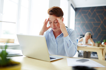 Fototapeta premium Tired or pensive woman sitting in front of laptop and preparing for report