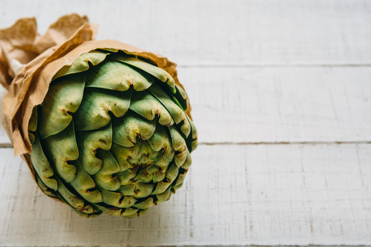 Close-up of artichoke wrapped in brown paper against a white background
