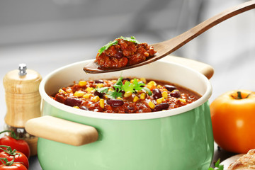 Wooden spoon with delicious chili con carne over saucepan on table