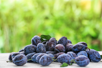 Tasty ripe plums on wooden table outdoors