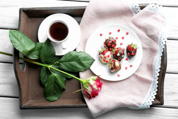 Tray with cup of tea, tasty glazed strawberries and beautiful flower on wooden background