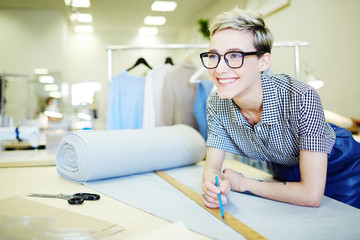 Young shop assistant of sewing department measuring piece of fabric for client