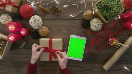 Top view hands tie a bow using digital tablet at wooden desk from above with christmass decoration - Powered by Adobe