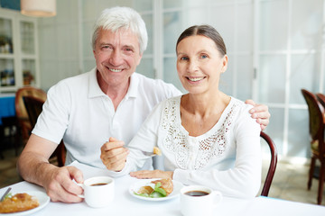 Affectionate senior spouses having tasty dessert with coffee in cafe