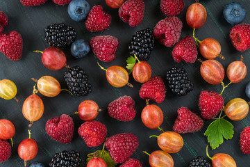 different fresh berries, mixed on the black-green background of the table