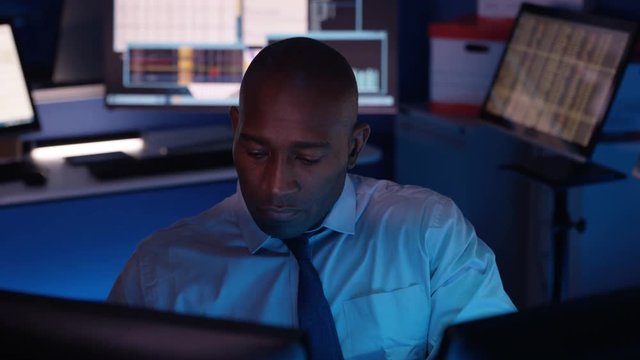  Computer expert working in a dark room surrounded by computer screens