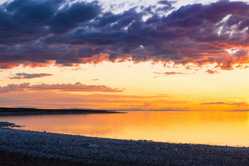 dark fluffy clouds on sun-drenched sky over sea during fiery sunset  
