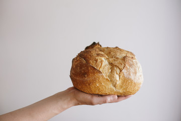 Close up of a hand holding a round artisanal bread with white background