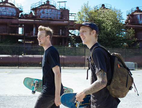 two young men walk together with skateboards