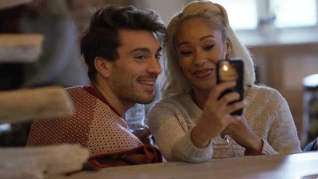  Happy couple relaxing in front of open fire, pose to take selfie with phone	