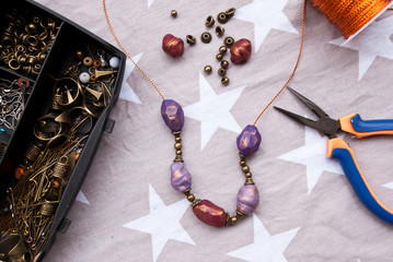 Assembly of jewelry of polymer clay in bohemian style with gold elements and box with small beads. Hobby, handicraft. Pilers with unfinished necklace.Trend color bordo.