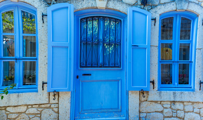 Obraz premium View of Tourquaz,Turquoise color wooden door and window with white stone wall background in Alacati,Turkey.