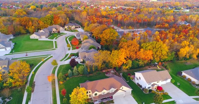 Tranquil idyllic neighborhood amid colorful Autumn trees at dawn, aerial view.
