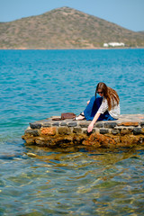 young beautiful girl sitting on a pier looking at the sea and mountains