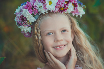 Cute blond girl with blue eyes close portrait wearing wild flowers wreath on top head smiling and looking to camera with eyes full of love joy and life.