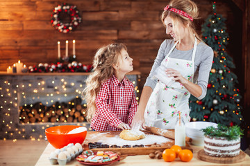 Merry Christmas and Happy Holidays. Family preparation holiday food. Mother and daughter cooking cookies in New Year interior with Christmas tree.