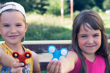 Portrait of two funny friends playing with colorful fidget spinners on the playground. Popular...