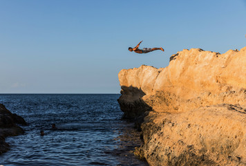 Young man jumping from rock to sea.