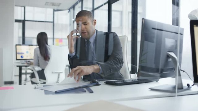 Businessman working on computer in the office gets bad news from phone call. 
