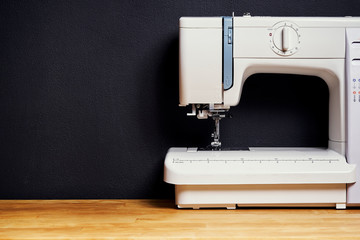 white sewing machine on a bright wooden table and a black wall