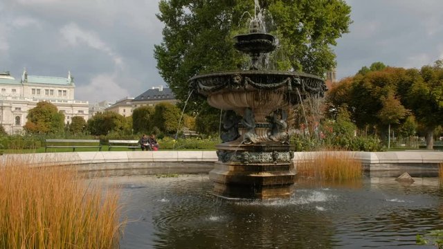 Camera slides past plants to reveal beautiful fountain in Volksgarten Vienna. Taken on a sunny September morning 