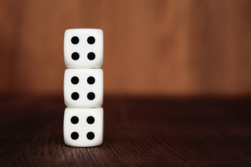 Three white plastic dices on each other on brown wooden board background. Six sides cube with black dots. Number 444.