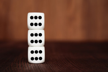 Three white plastic dices on each other on brown wooden board background. Six sides cube with black dots. Number 666.