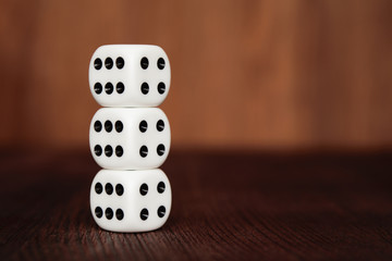 Three white plastic dices on each other on brown wooden board background. Six sides cube with black dots. Number 4 and 6.