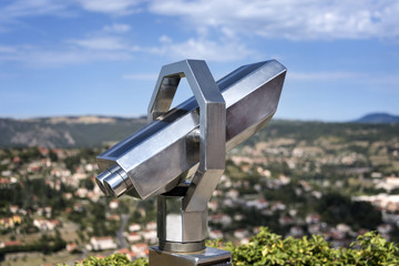 Silver metal touristic telescope on a viewing desk with blurred cityscape and horizon in the background
