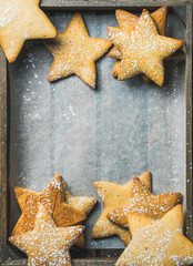 Sweet Christmas holiday gingerbread cookies in shape of stars with sugar powder on baking paper in rustic wooden tray, top view, copy space, vertical composition