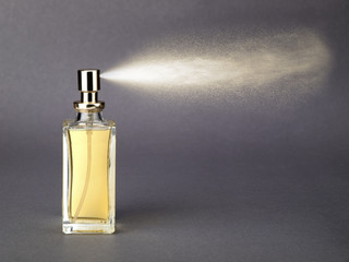 Bottle of golden colored perfume with spray jet on gray background