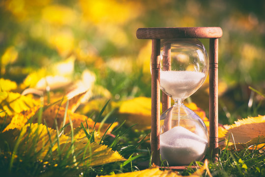 Hourglass In Fallen Leaves. Time Is Passing Fast During Autumn Season. Time And Season Concept. 