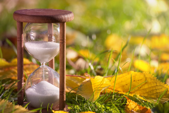 Hourglass in fallen leaves. Time is passing fast during autumn season. Time and season concept. 