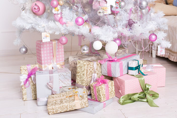 Giftboxes, pink and white christmas decorations balls hanging on a decorative white christmas tree.