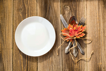 Thanksgiving dinner plate with fork, knife and autumn leaves on rustic wooden table background. Top view, copy space