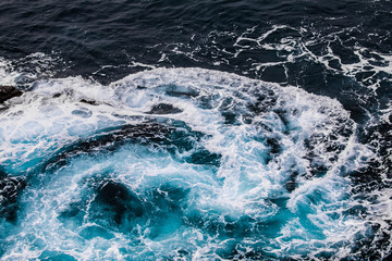 vertiginous, swirling foamy water waves at the ocean photographed from above