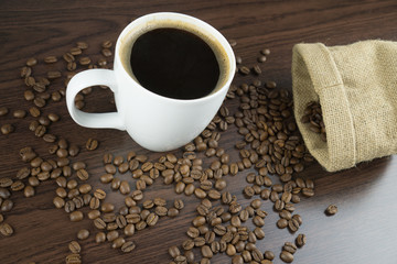 White cup of hot coffee with coffee beans on wooden brown background