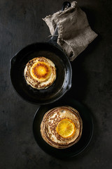 Homemade pancakes with fried orange, served in cast-iron pan and black plate on dark background. Top view with space