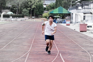 Young healthy Asian man running on racetrack at athletics stadium.