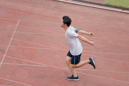 Athletic handsome young Asian runner sprinter crossing the finish line on track in stadium.